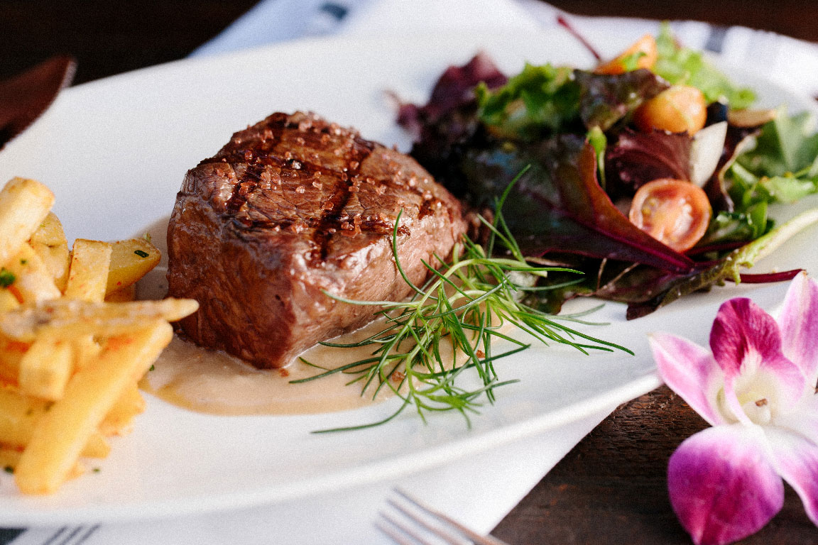 photo of a steak dinner with fries, salad, and a flower